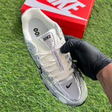 White Nike sneaker held by a gloved hand on grass with a red Nike box in the background