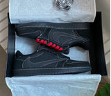 A pair of black Nike Air Force 1 Low sneakers with red laces and white contrast stitching, presented inside their black shoebox with white tissue paper.